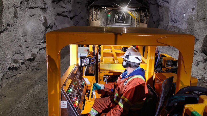 An underground mine worker operating an electric piece of machinery.
