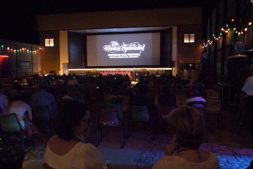 An audience at an outback open-air cinema watches a film on the big screen.