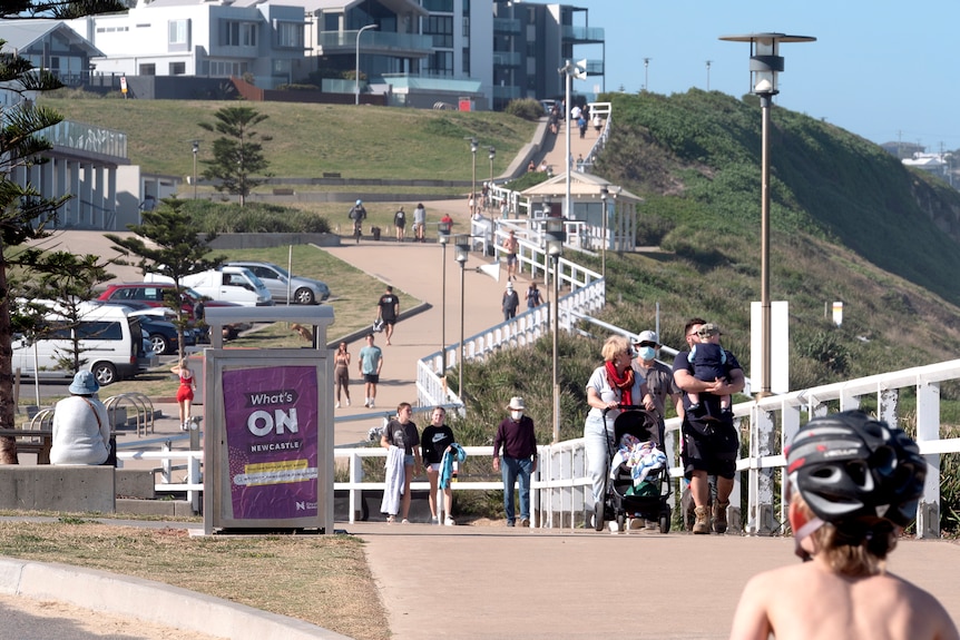 A wide shot of people walking on a path near the beach with some wearing masks