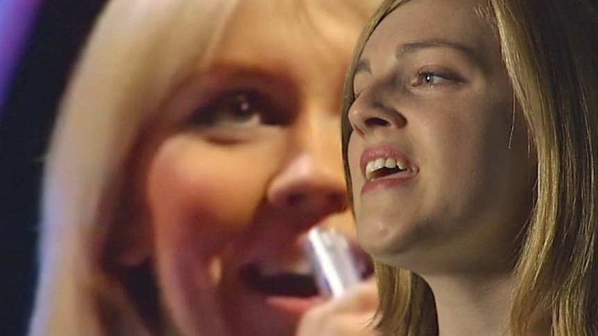 Hobart university student Grace McCallum sings in front of a television screen showing ABBA singer Agnetha.