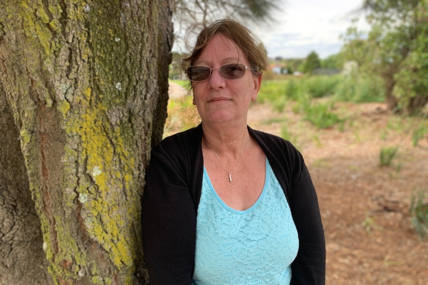 A woman leans against a tree trunk. 