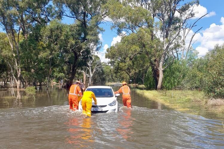 Three SES volunteers in orange jumpsuits push a car along a completely flooded road. 
