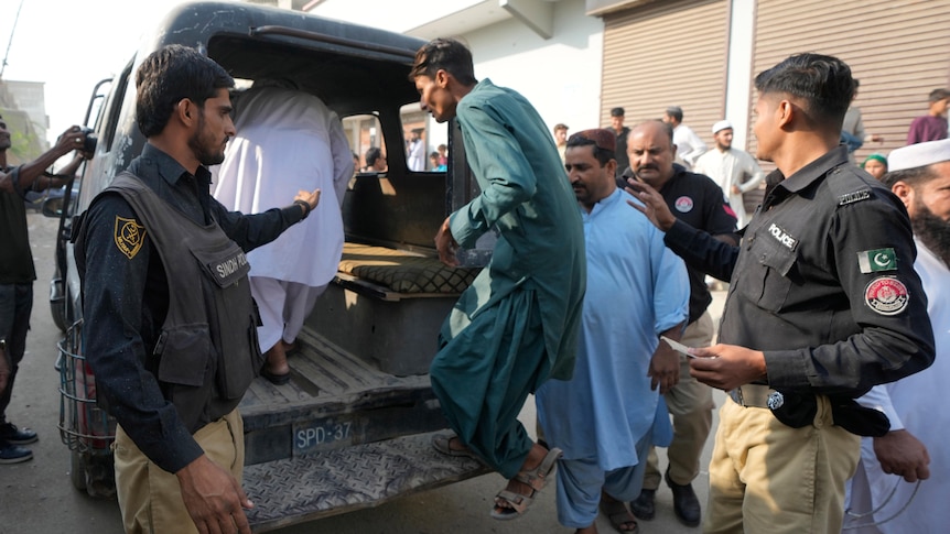 Uniformed Pakistani police officers detain Afghan immigrants and load them into the back of a small police van.