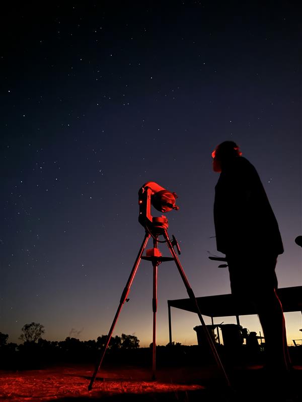 Man wearing red headlamp testing astronomy equipment at dusk