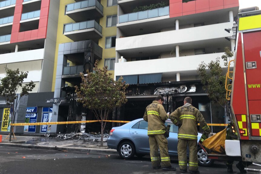 Two firefighters and a truck at the scene of a restaurant fire at the base of an apartment block.