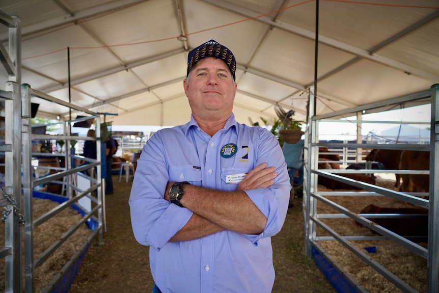 A middle-aged man in a cap stands with his arms folded in a stockyard.