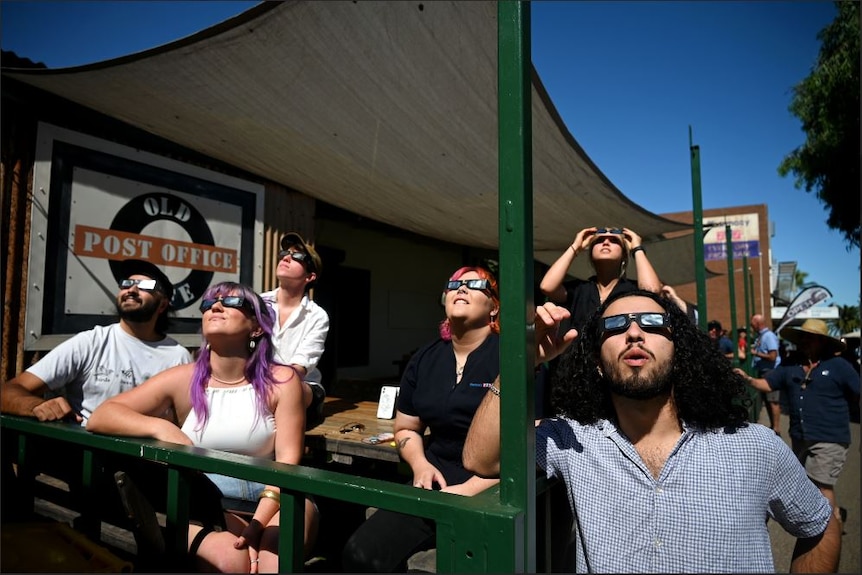 People wearing eclipse glasses sitting on a balcony and watching the sky.