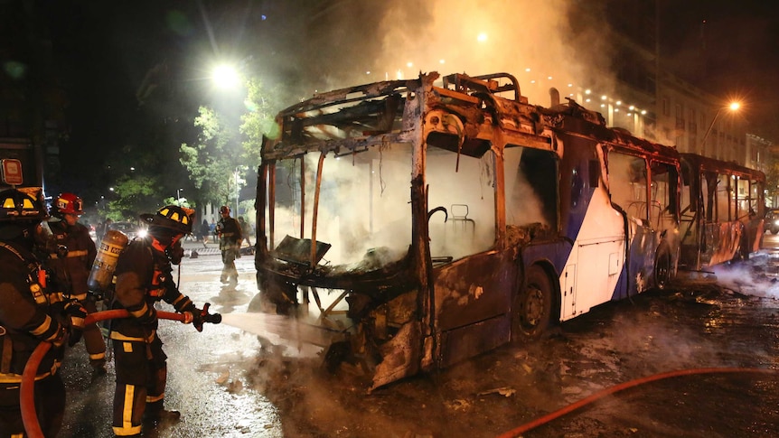 At night, firefighters hose off the charred remains of a public bus.