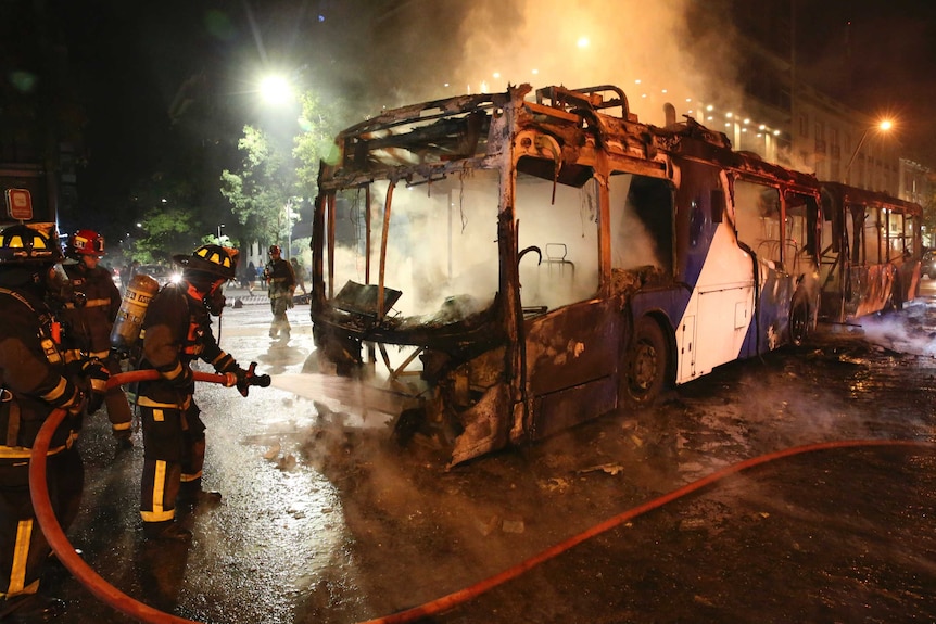 At night, firefighters hose off the charred remains of a public bus.