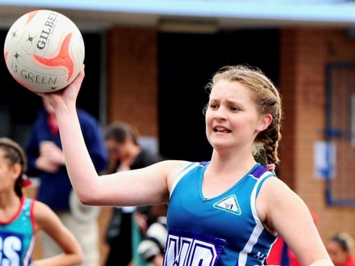 Teenage girl holds a netball during a game, looking determined.