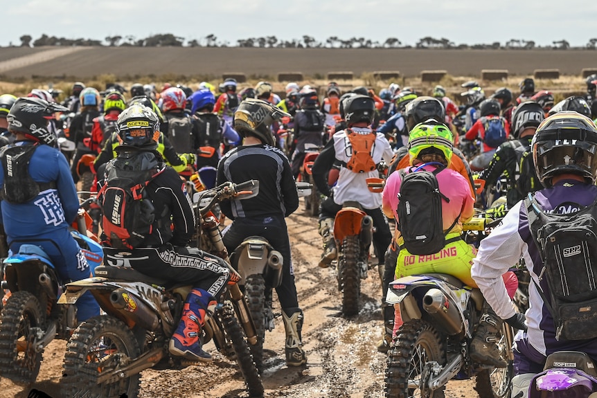 Backview of large group of motorbike riders in dirt paddock