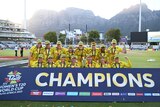 The Australian women's cricket team stands and crouches in front of a 'Champions' sign, with Table Mountain in the background.