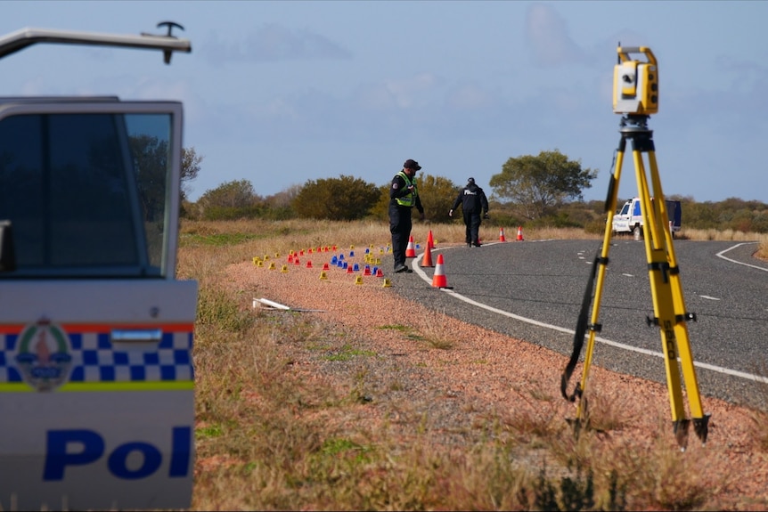 Police inspect the side of a highway in the Central Australian outback, near some road markers and a police vehicle.