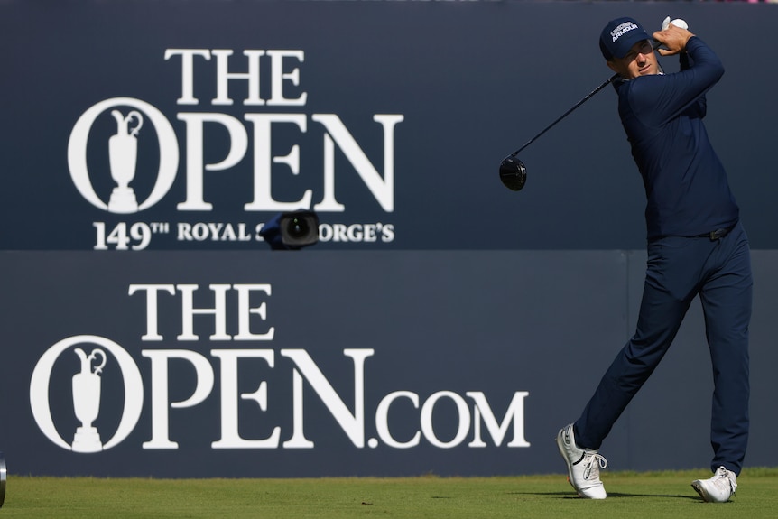 American golfer Jordan Spieth finishes his swing on a tee-shot, with a sign behind him for the Open Championship. 