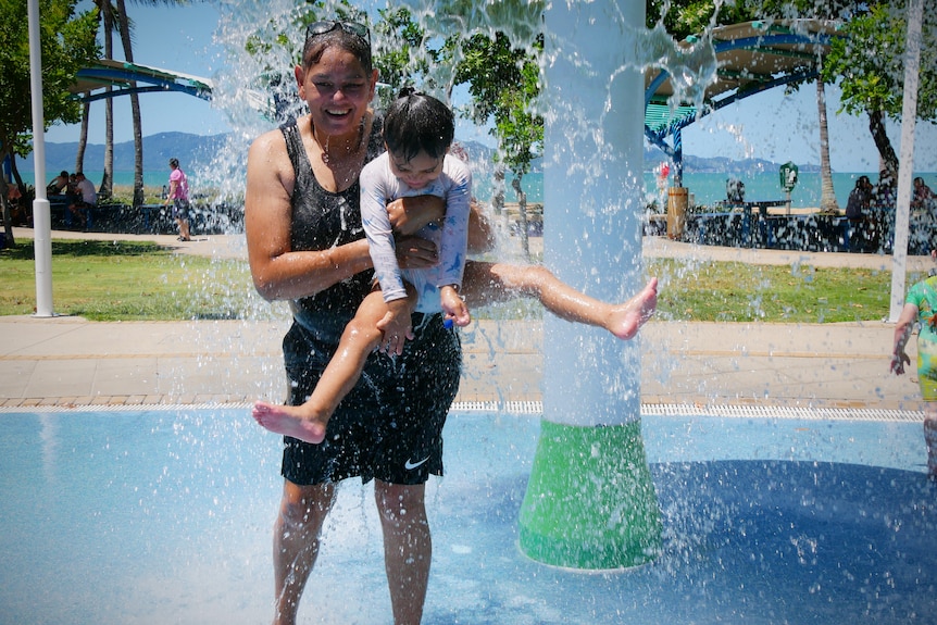 A woman holds a young girl in the air at a water park 