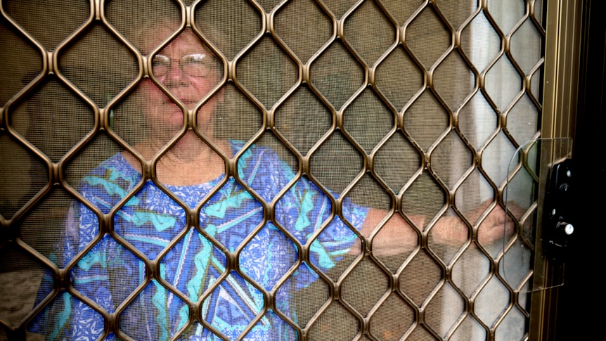 Woman looks out, the bars of the flyscreen door blocking her