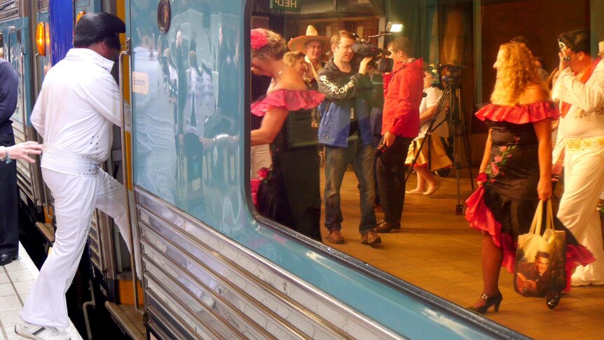 An Elvis impersonator walks onto the Elvis Express, with fans and other impersonators reflected in the train window.