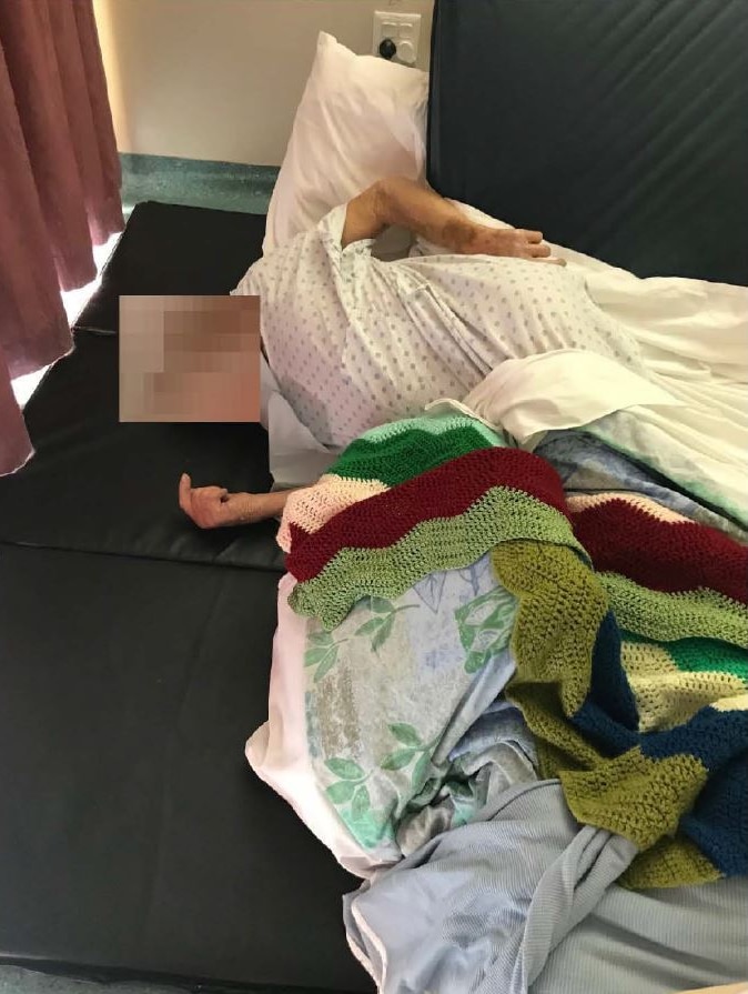 A photo of an 85-year-old man lying on mattresses on the ground in a regional Queensland aged care facility.