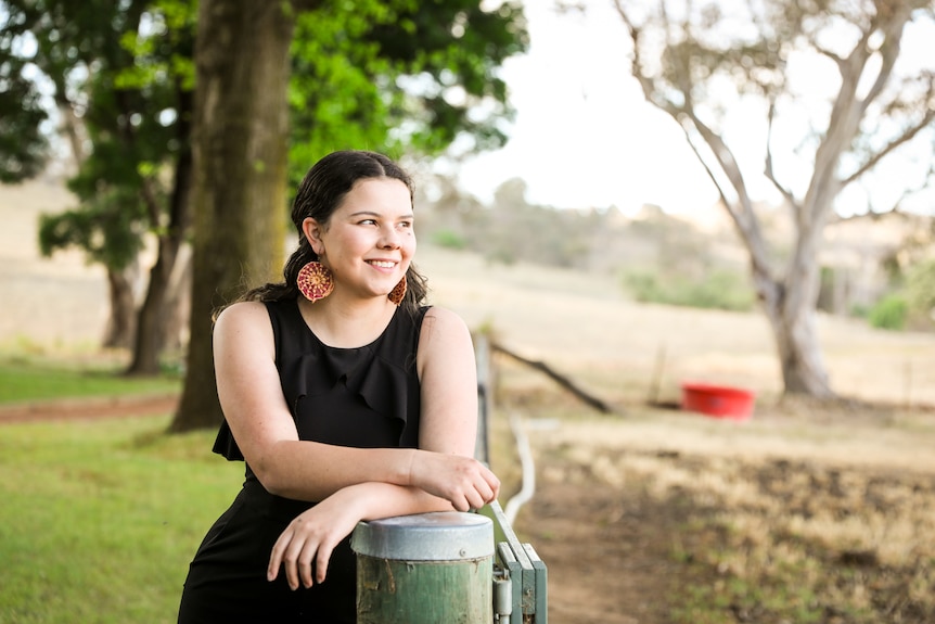 Dhani Gilbert leans on a fence post on a farm.