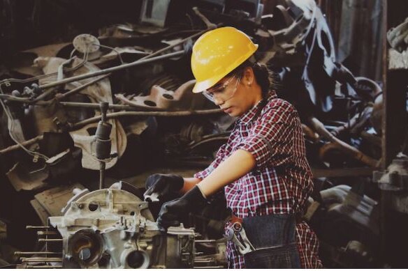 Female employee wearing hard hat, goggles works in a mechanical setting