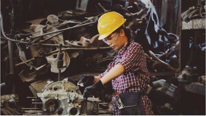Female employee wearing hard hat, goggles works in a mechanical setting
