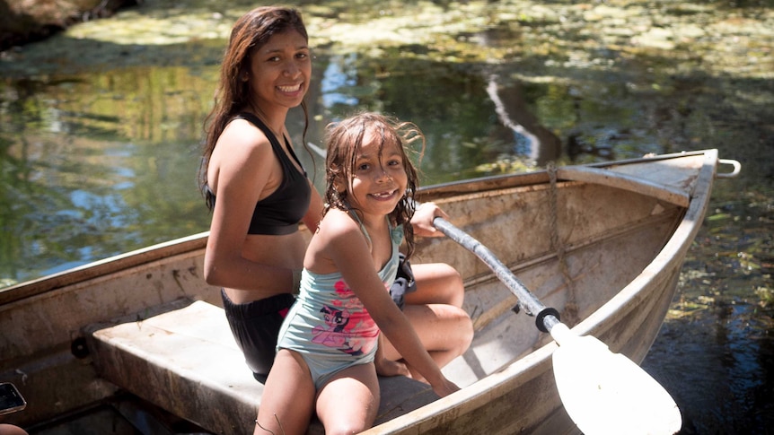A teenager and a young girl smile sitting in a boat in a water hole in the Kimberley.