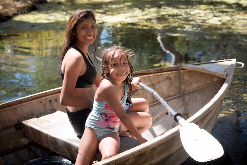 A teenager and a young girl smile sitting in a boat in a water hole in the Kimberley.