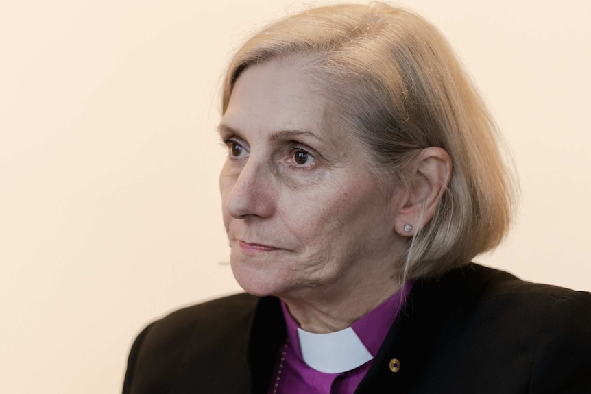 A woman looks to the left of the frame against a cream backdrop.