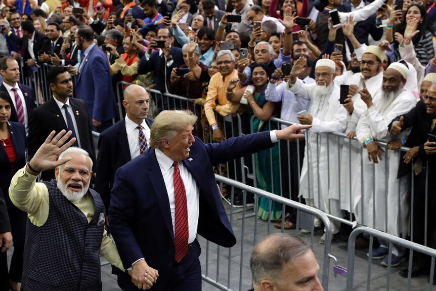 President Donald Trump and Indian Prime Minister Narendra Modi hold hands and walk past a crowd of people waving