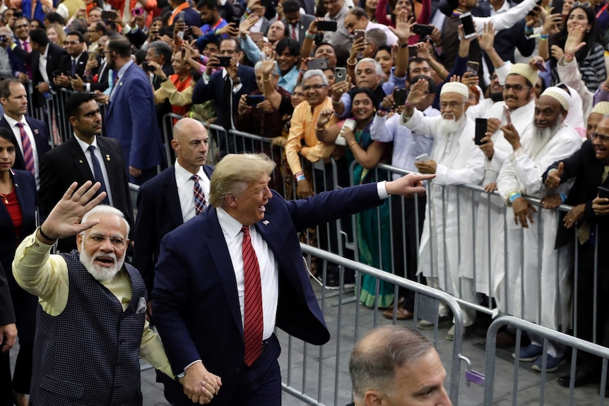 President Donald Trump and Indian Prime Minister Narendra Modi hold hands and walk past a crowd of people waving