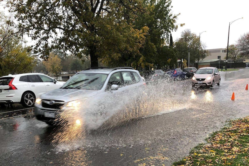 A spray rises as cars drive past puddles on a road under grey skies in Ballarat.