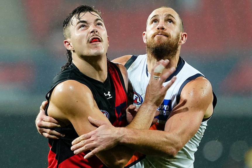 An Essendon AFL players and a GWS opponent push against each other as they prepare to contest for the ball.