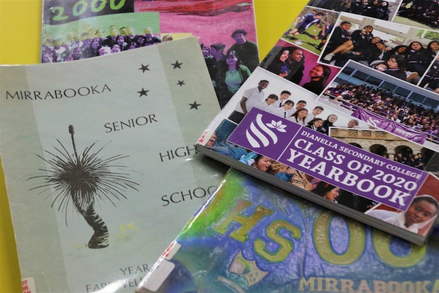Several archived year books on a table, with colourful photos and writing on them.