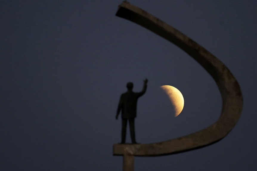 the moon is seen behind a statue of a man