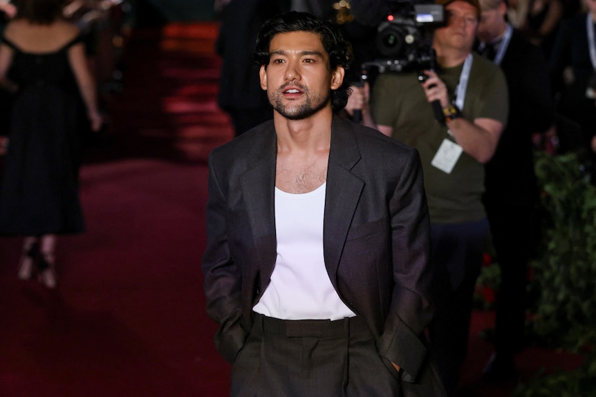 A man with dark hair, white t shirt and black suit
