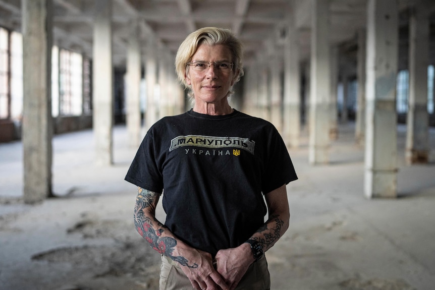  Medic Yuliia Paievska stands facing the camera in an abandoned-looking building with her hands interlocked. 