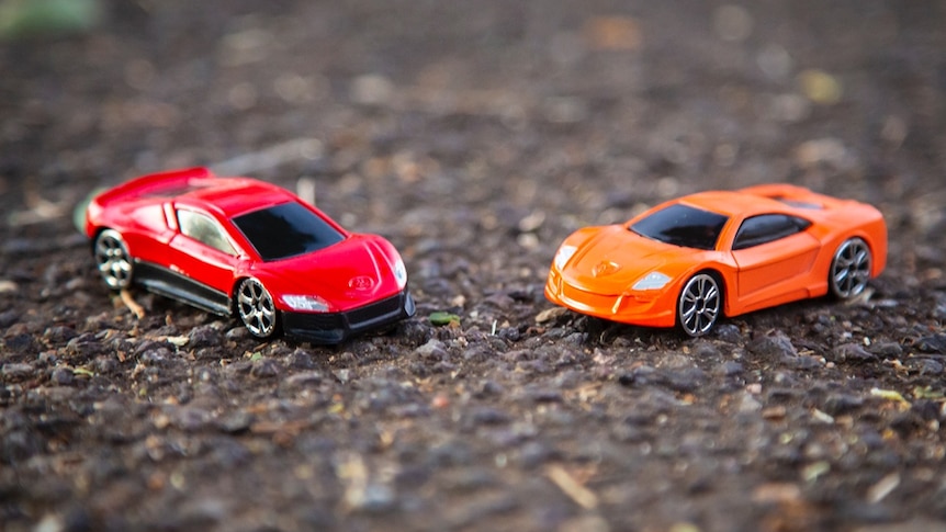 Toy cars face each other on asphalt.