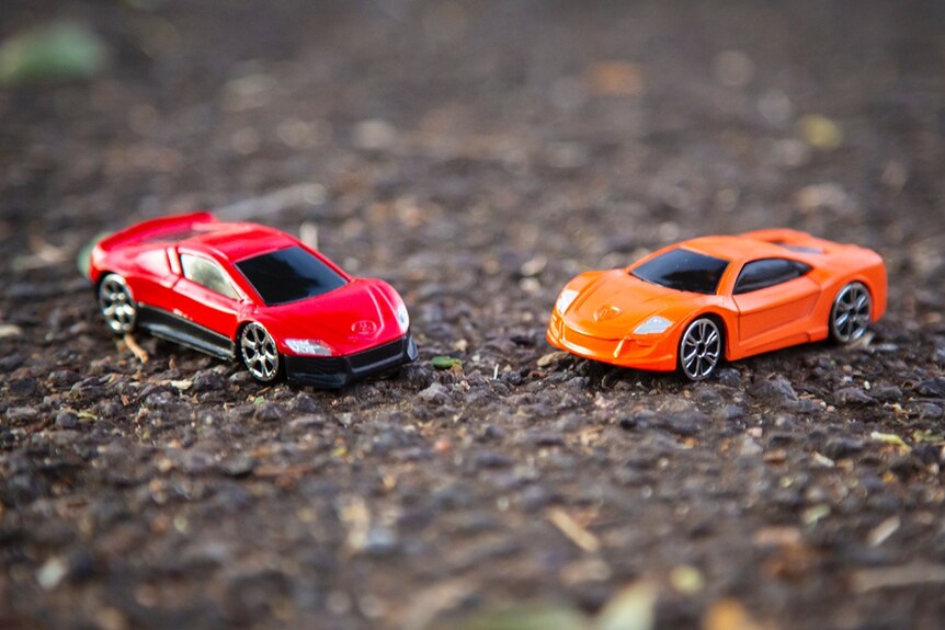 Toy cars face each other on asphalt.