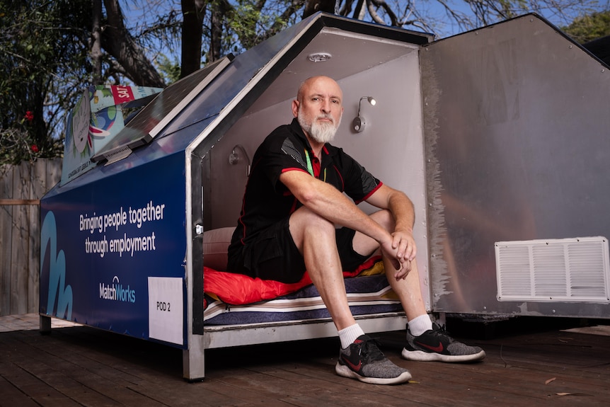 A man sits in the entrance to a sleeping pod.
