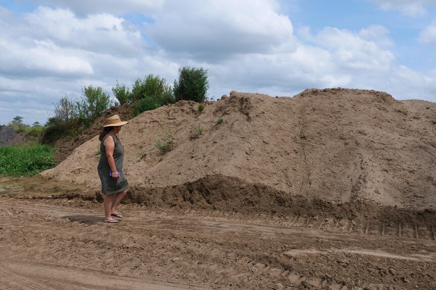 A woman stands next to a large pile of sand