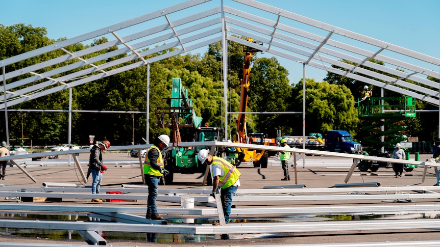 Workers assemle a structure in a car park. 