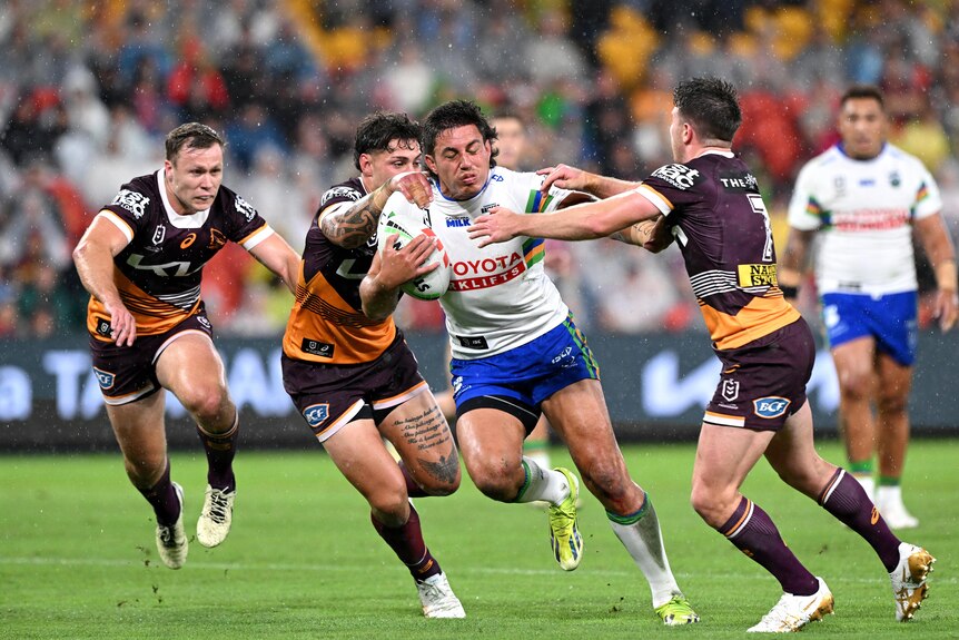 An NRL player runs with the ball, as three opponents attempt to tackle him