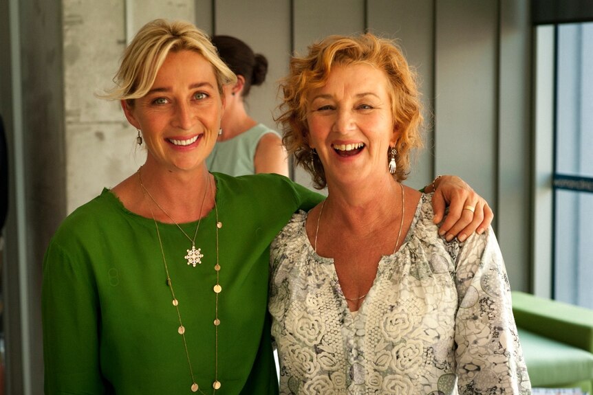 Actress Asher Keddie stands in a green top to the left, she has her arm around Debra Owald in a white top, both are smiling.