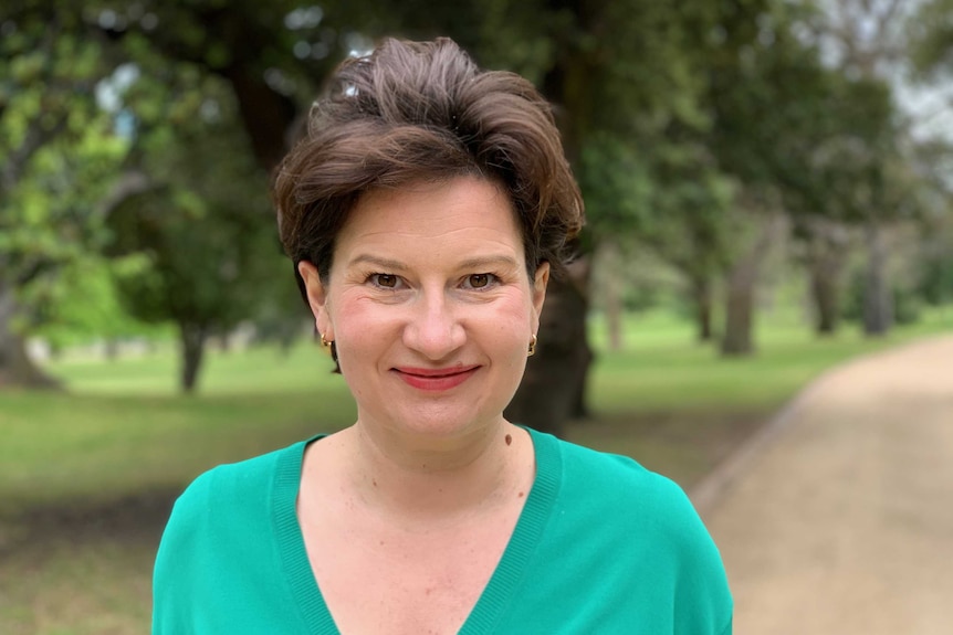 Sarah McNamara stand in a park and smiles at the camera.