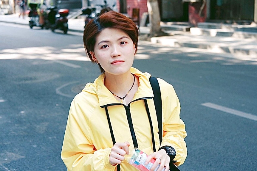 Wuhan resident Yu Yi, a college teacher, with short hair and wearing a yellow jacket, holding a bottle of water.