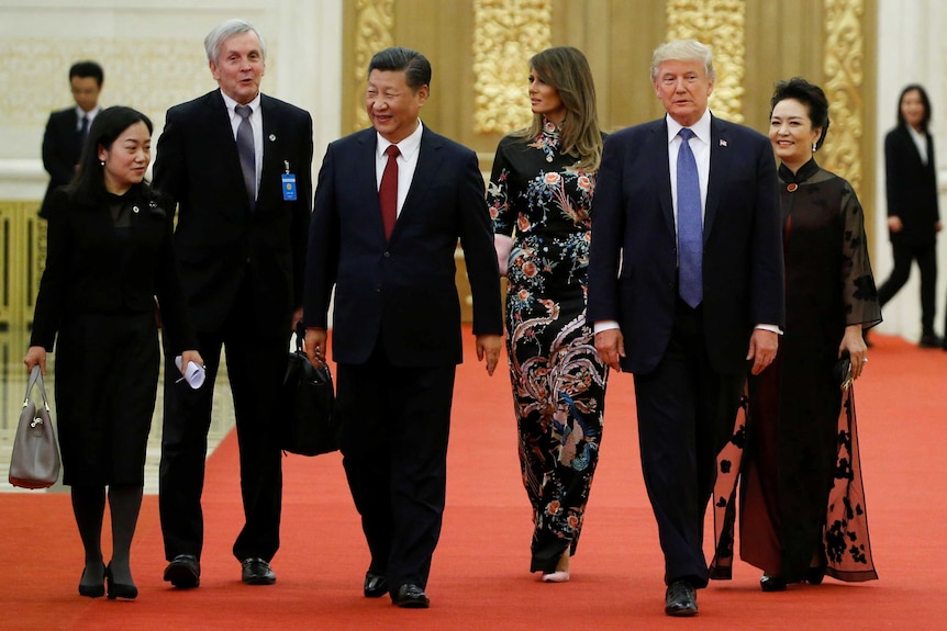 Donald Trump, Melania Trump, Xi Jinping and Peng Liyuan walk side-by-side on red carpet.