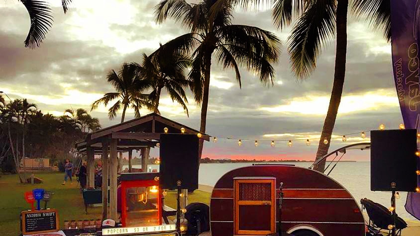 Outside stage and teardrop caravan set up by the beach.