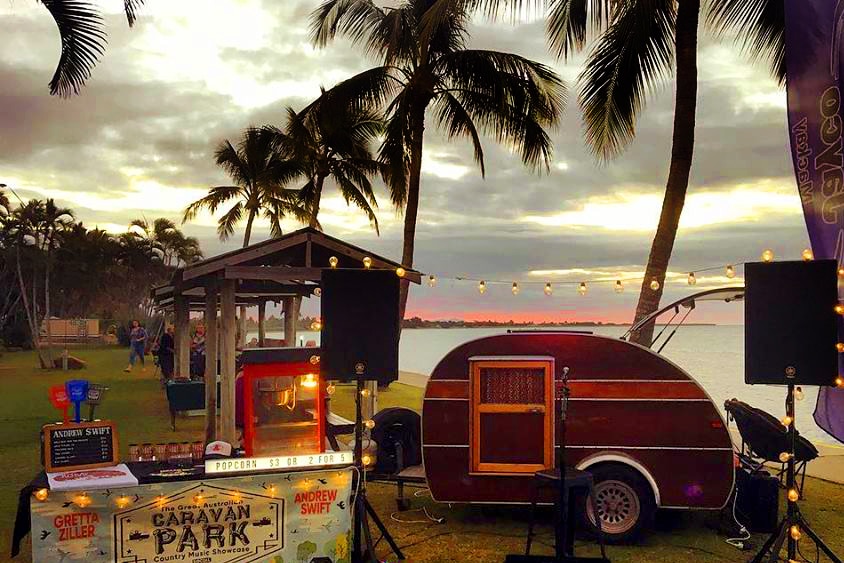 Outside stage and teardrop caravan set up by the beach.
