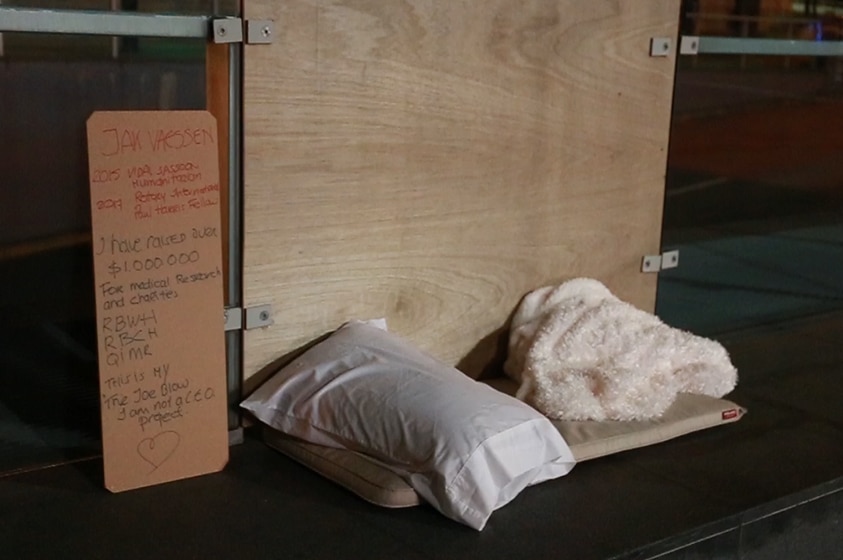 A blanket, pillow, mat and sign on a concrete path in Brisbane CBD.