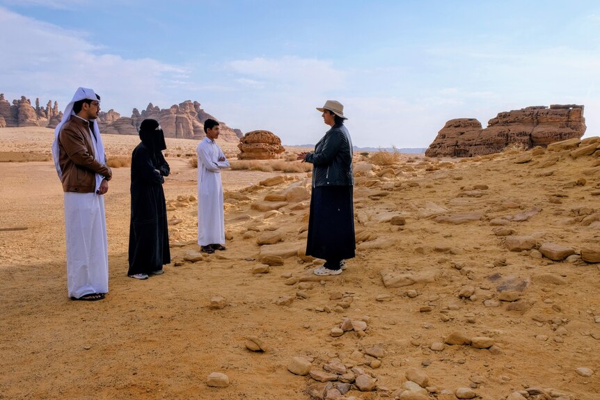 A female tour guide speaks to a Saudi family in traditional dress.